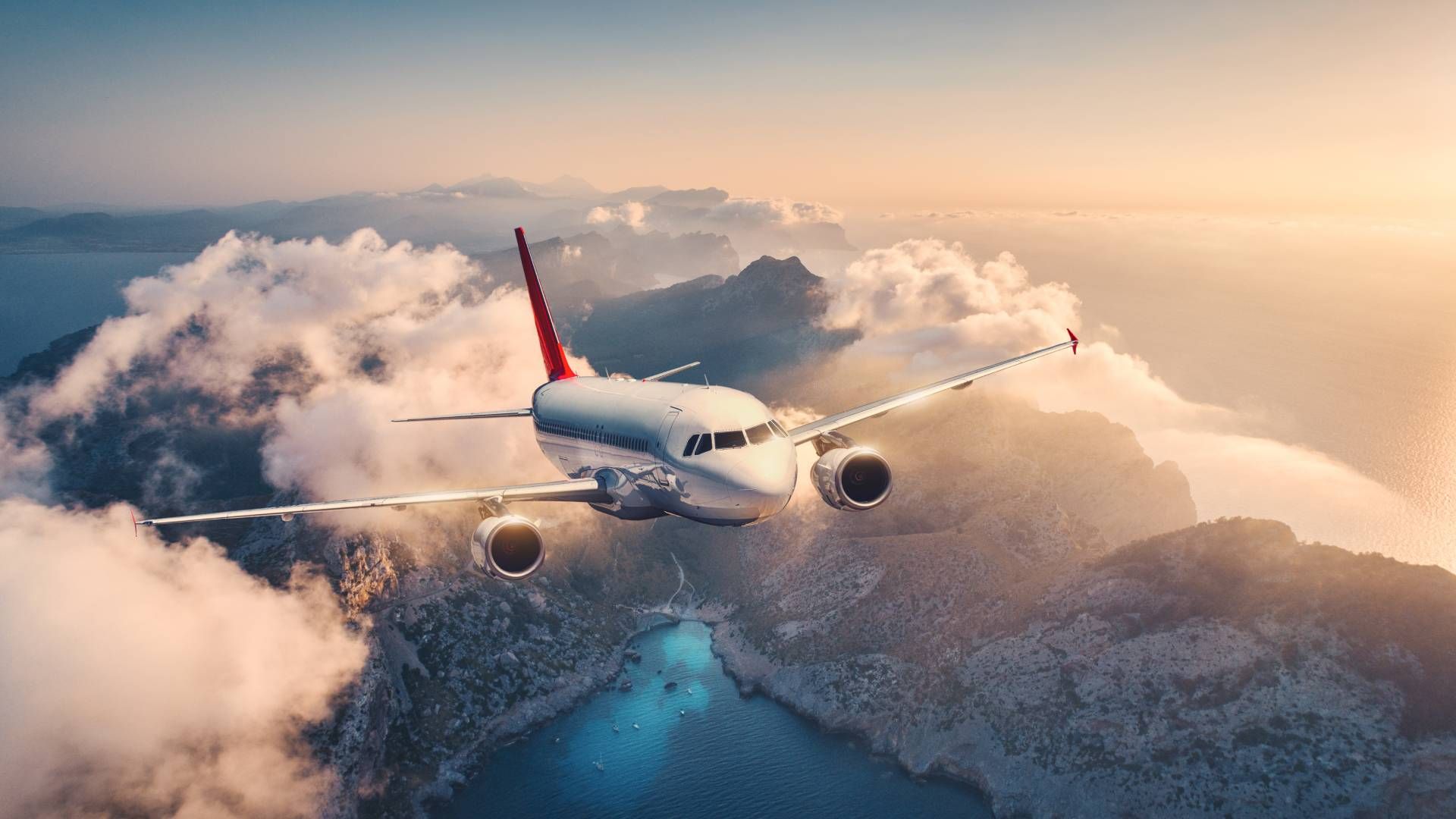 Airplane flying above a layer of clouds over mountain peaks